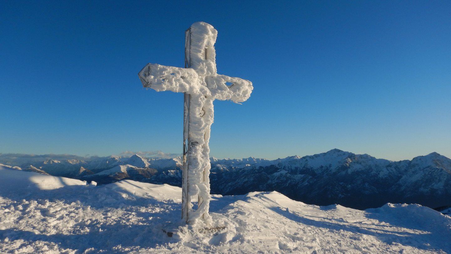 La croce si staglia sul cielo azzurro in contrasto con la neve bianca