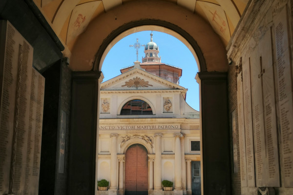 View of Piazza San Vittore from Corso Matteotti through the Arco Mera in Varese. A lady strolls in broad daylight in front of the Basilica of San Vittore in Varese